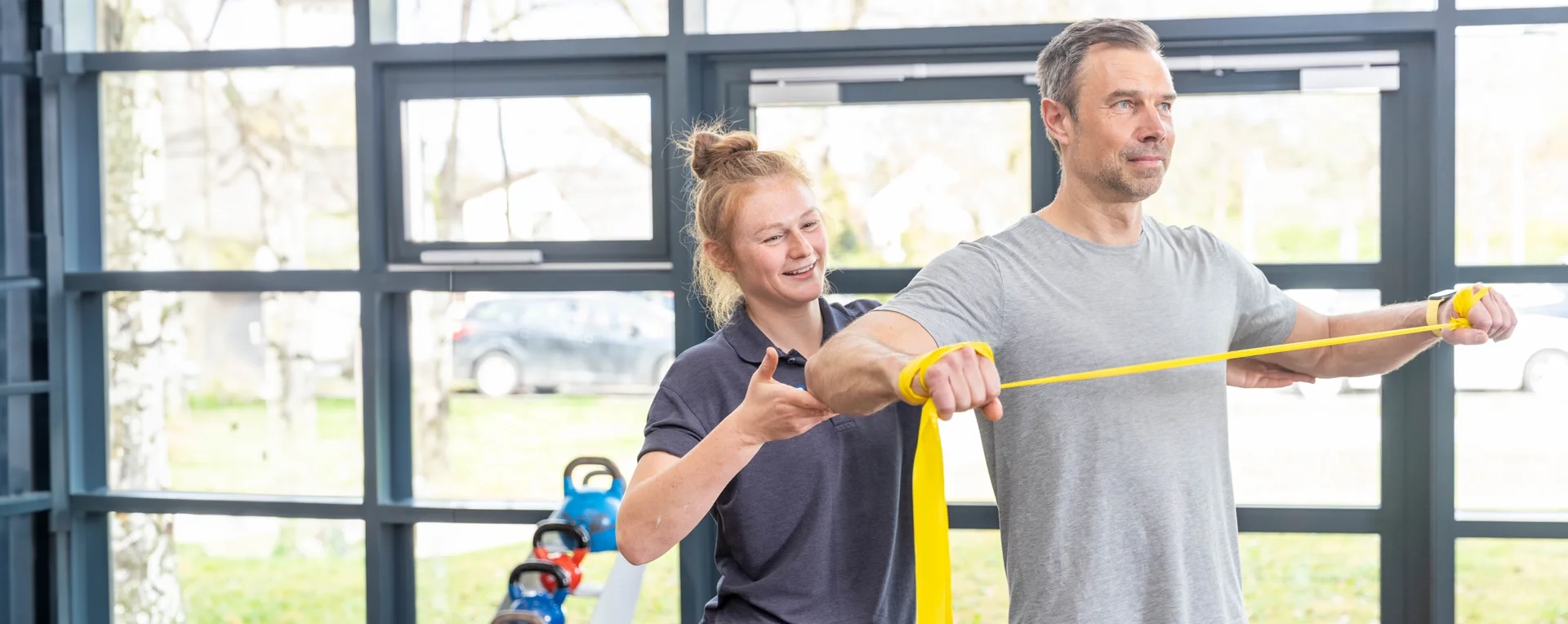 DianaKlinik | Leitbild Eine Physiotherapeutin unterstützt einen Patienten bei einer Reha-Übung mit dem Theraband.