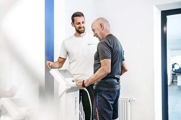 Ein Sporttherapeut von DianaMedicalSport erläutert einem älteren Mitglied die Daten auf der Körperanalysewaage.